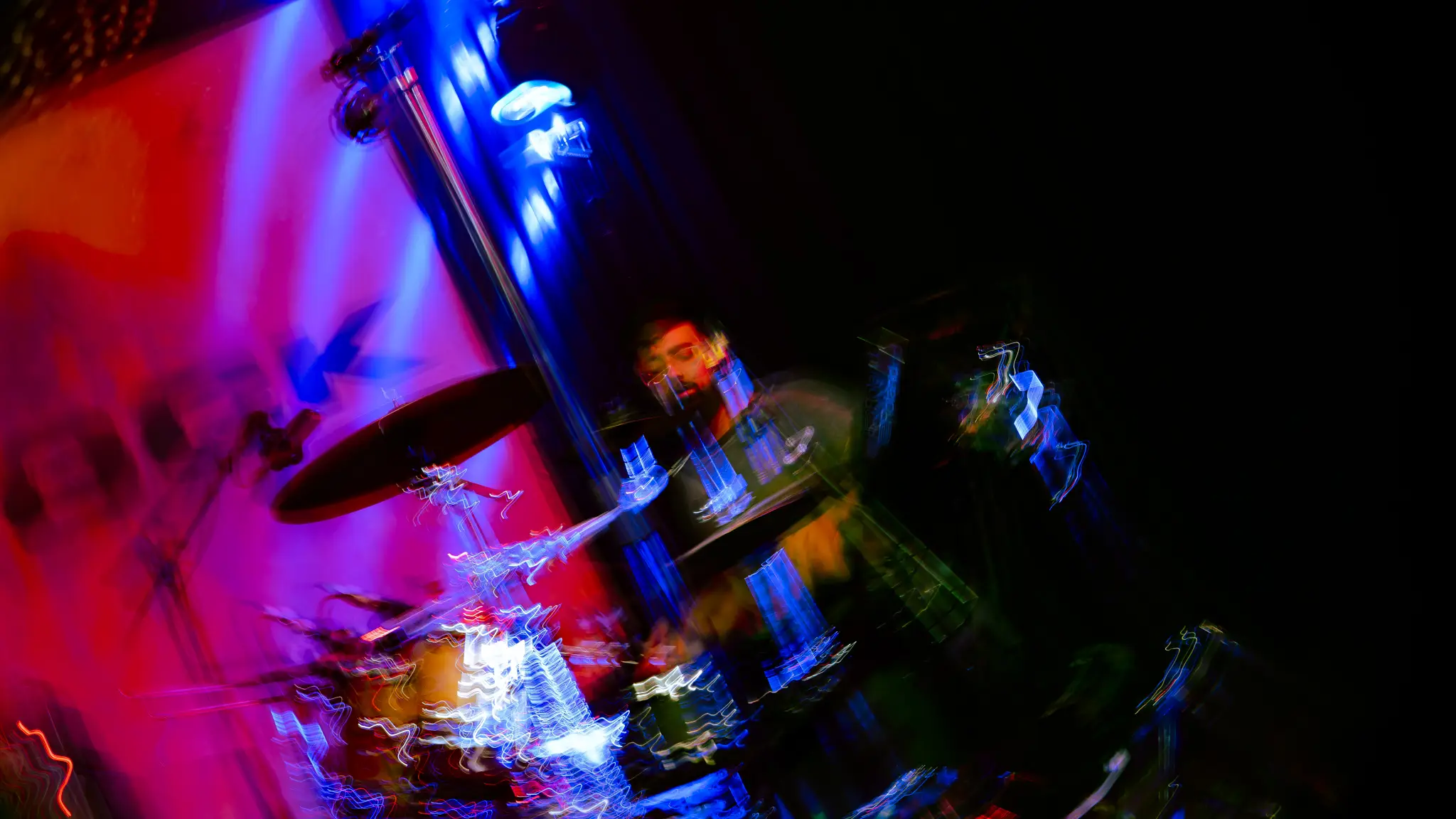 The drummer mid-fill, arms blurred, under neon light