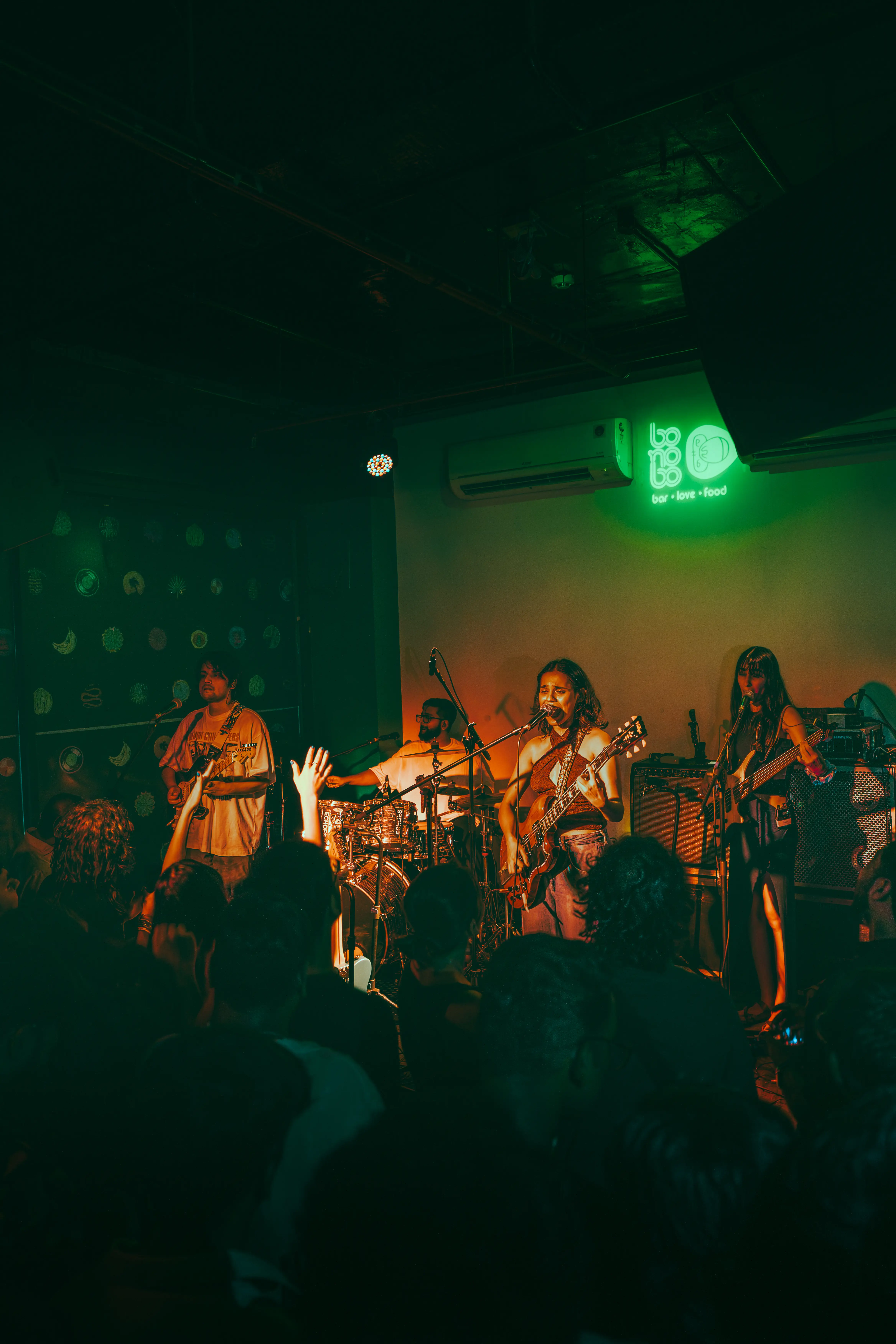 A packed club crowd in green light, the band on stage beyond