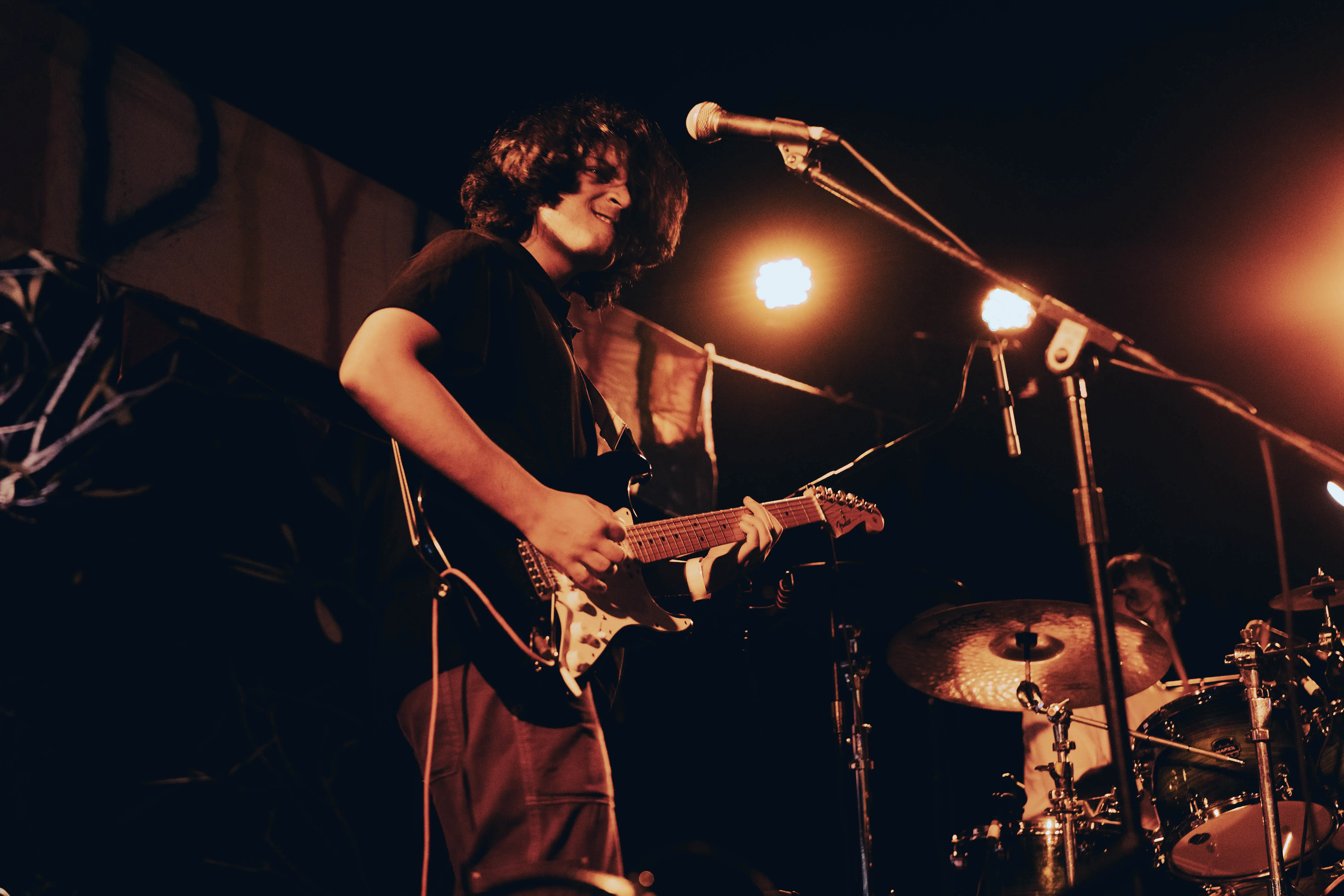 Guitarist grinning mid-song in an amber spotlight